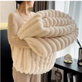 Personne tenant une couverture blanche pliée, à texture duveteuse et reliefs en larges bandes. 
